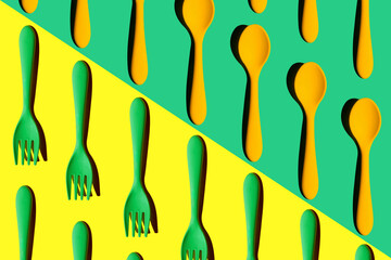 a pattern of green plastic forks and yellow spoons on a yellow-green background with a hard light, top view