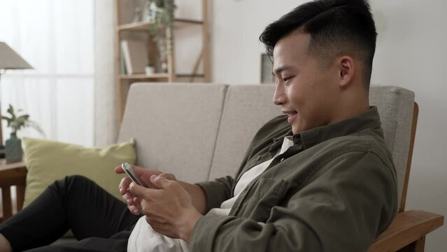 closeup view of smiling asian man having fun texting message and zooming pictures while using chap app on the phone in the living room at home.
