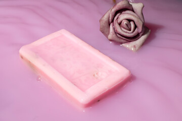 Natural rose soaps and an artificial pink rose in pink liquid.
