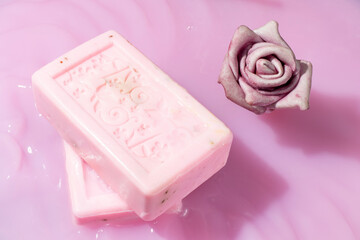 Natural rose soaps and an artificial pink rose in pink liquid.