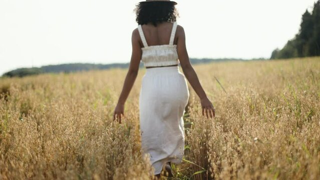 4k video african-american woman in the wheat field. African female in white clothes and hat running in the countryside.