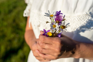 woman in a white dress holds a bouquet of wildflowers in her hands