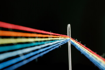 multi-colored threads for sewing in the form of a rainbow pass through an antique needle on a black...