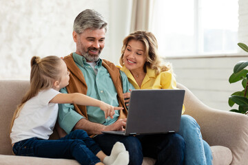 Family Of Three Using Laptop Computer Sitting On Sofa Indoors