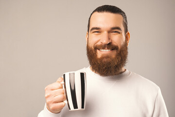 Close up portrait of a bearded man holding a mug and smiling at the camera.