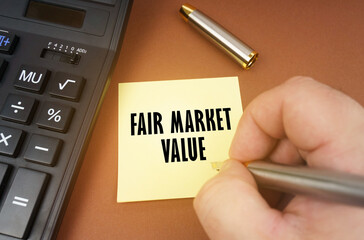 A calculator lies on a brown surface, a hand with a pen makes an inscription on a sticker - Fair...