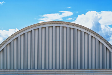 Side view of a gray metal hangar with a round roof against a blue sky. Profile stripes are visible...