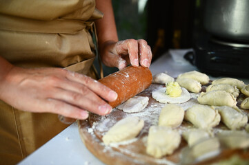 Selective focus. Close-up of a chef using a rolling pin, rolls out dough on a wooden board, prepares homemade dumplings