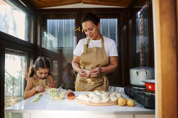 Beautiful woman, loving young mother and her cute little daughter kneading dough and cooking...