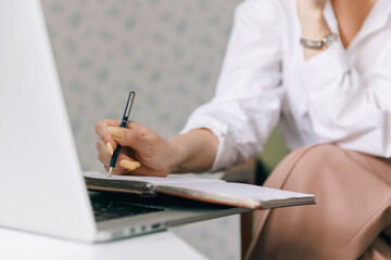 Closeup woman psychotherapist is holding notebook and making notes during online therapy session,...