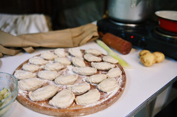 Homemade dumplings, Ukrainian varenyky on a wooden board, sprinkled with flour and a pot with boiling water on the stove