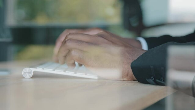 View behind glass unknown afro businessman leader boss programmer IT specialist trader typing on modern wireless keyboard using computer in office for chatting with business partners develop software