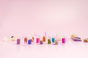 Manicure broths of different colors in small bottles stand in a row on a pink background