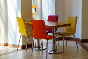 Upholstered yellow and red chairs stand around a square table in the building.