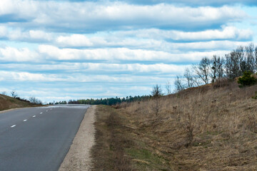 An empty roadway outside the city passes by a rural field and a blooming meadow. Travel by car away...
