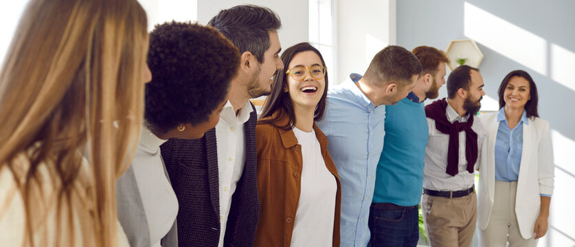 Multiracial Group Of Happy Business People All Together Having Fun In Office. Diverse Team Of Positive Young Men And Women Standing In Row, Hugging Each Other, Laughing And Smiling. Teamwork Concept