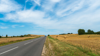 An empty roadway outside the city passes by a rural field and a blooming meadow. Travel by car away from the city and the hustle and bustle. Paved road on a sunny day without cars.