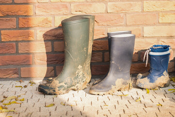 Three dirty boots of all family members. Boots of child and parents. In the fall there is a lot of work in the garden. Children help with gardening. Lot of mud on the boots. © Matej
