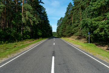 A new modern asphalt road passing through the forest. An empty country road in the woods. High-quality conditions for cargo and passenger transportation.
