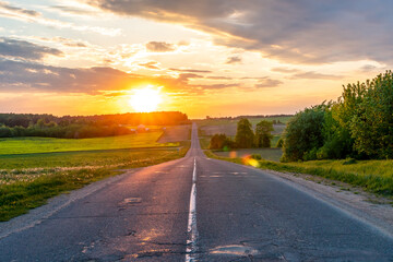 Beautiful sunset over an empty road in the countryside. An empty asphalt road runs along a field and forest during sunset.