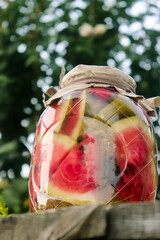 pickled pieces of red watermelon in a glass jar on a wooden table in the garden in summer selective...
