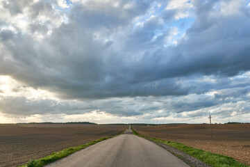 An empty roadway outside the city passes by a rural field and a blooming meadow. Travel by car away...