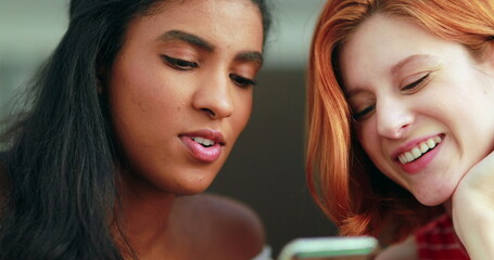 Two pretty multi-racial girls looking at cellphone screen, real laugh and smile