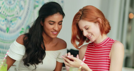 Two multiracial girls looking at cellphone screen laughing and smiling