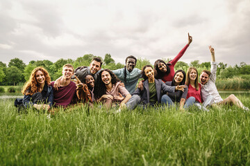 Portrait of young multiracial freedom friends cheering and having fun resting on the grass -...