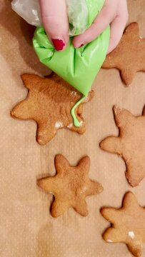 Close-up of person baking homemade christmas cookies with icing. Person adding green icing to star shaped gingerbread cookies. High-angle view. Vertical footage.