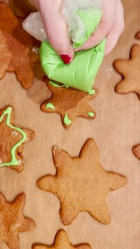 Baking homemade christmas cookies with icing. Person adding green icing to star shaped gingerbread cookies. High-angle view. Vertical footage.