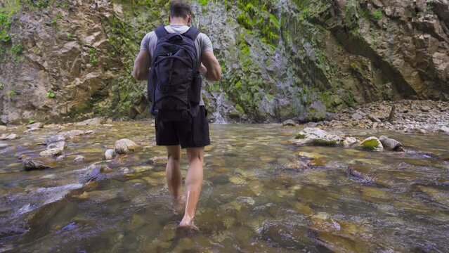 Man walking barefoot in stony creek. There is a waterfall.
Man walking barefoot in the stream, walking towards the waterfall.
