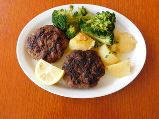 Grilled beef patties served with potatoes, lemon and broccoli