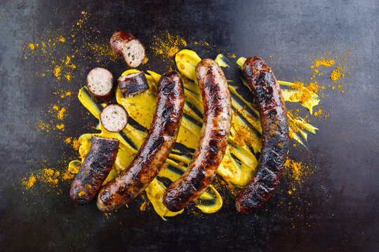 Barbecue Allg&auml;u bratwurst served with hot mustard and curry as top view on a rustic old board