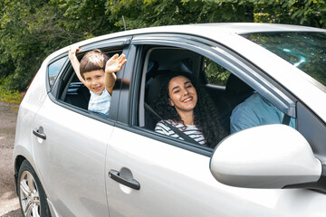 Happy cheerful millennial arab family with boy go to vacation by car at summer, kid waves his hand out the window