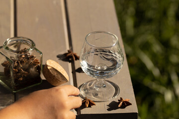  crystal glass with aniseed liqueur, rum, tequila with aniseed seeds, jar with cork lid, grey wooden table and grass background, text space