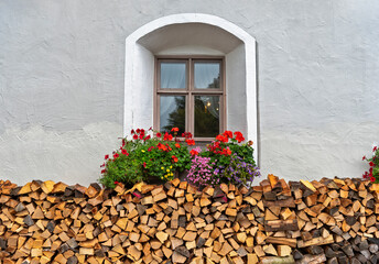 Ein Stapel Brennholz unter einem Fenster mit bunten Blumen