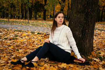 Girl sits under a tree with books in autumn on yellow foliage