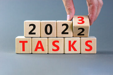 2023 tasks new year symbol. Businessman turns a wooden cube and changes words Tasks 2022 to Tasks 2023. Beautiful grey table grey background, copy space. Business 2023 tasks new year concept.