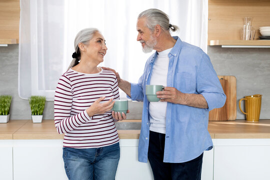 Happy Senior Couple Drinking Morning Coffee And Chatting Together In Kitchen
