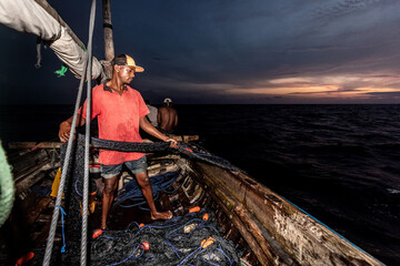 Night fishing. A man pulls out a fishing net at night. Indian Ocean