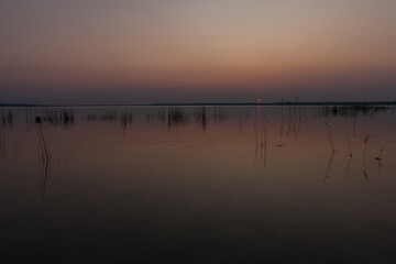 Sunset on the lake. Evening sky with beautiful solar disk is reflected in the water of the lake