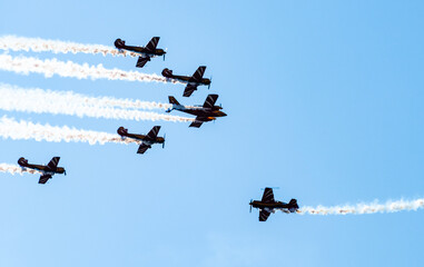Silhouettes of training aircraft performing aerobatics on a clear sunny day.