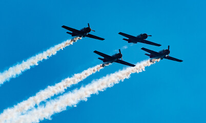 Silhouettes of training aircraft performing aerobatics on a clear sunny day.