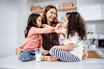 Obraz na płótnie Canvas Mother with two diverse daughters having fun drinking milk with cookies together in the kitchen, relationships with learning development and leisure activities for children.