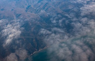 Fototapeta na wymiar a bird's-eye view of the mountains, a strip of ocean and clouds in the sky from an airplane window