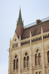 Fototapeta na wymiar Buildings in the Parliament House of Budapest, Hungary, are popular destination sites. Photo shows steep red roof line with embellished points and window with arches and round windows above.. 