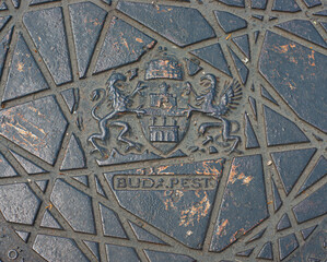 See closeup of a sewer hatch cover on the street in Budapest, Hungary, BUDA.PEST showing two cities and the coat of arms imprint.