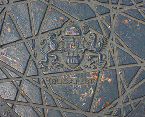 See closeup of a sewer hatch cover on the street in Budapest, Hungary, BUDA.PEST showing two cities and the coat of arms imprint.