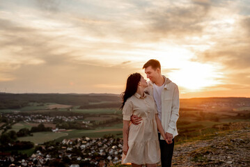 A couple in love, a guy and a girl are standing on a mountain at sunset hugging and kissing